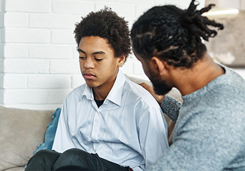 A concerned adult gently places a hand on the shoulder of a sad, withdrawn young boy. This image represents the crisis intervention services provided by Agency for Community Treatment Services, Inc. (ACTS) for juveniles experiencing crises due to intoxication or drug impairment, offering compassionate care and support during difficult times.